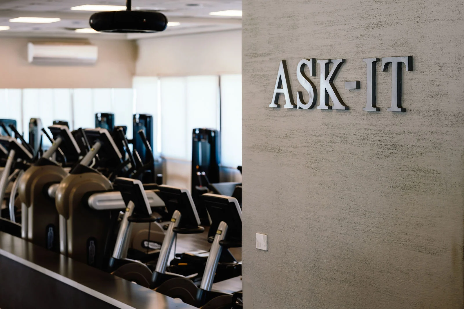 האותיות ASK-IT על קיר אפור, ולצידו שורת מכשירי אירובי